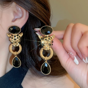 Detailed close-up of leopard-head earrings with emerald eyes and black teardrop pendants