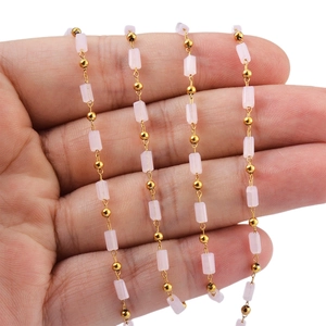 Gold stainless steel link chain with pink crystal beads held on a palm, white background