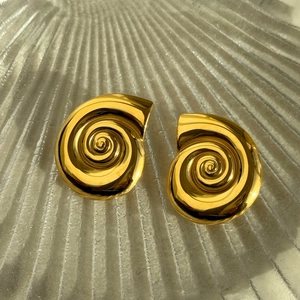Macro detail of high-polish gold conch spiral earrings on a textured glass surface
