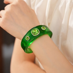 Detailed close-up of a vintage resin bangle with green gemstones and white rhinestones
