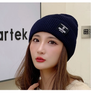 Detail of navy knit beanie featuring a black cloth label with MOMENT OF JBY lettering