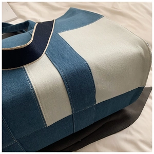 Close-up of color-block canvas tote bag featuring sky blue panels and white stitching details