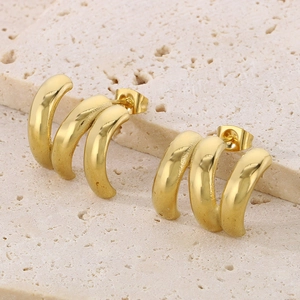 Detailed view of golden triple hoop stud earrings on a textured stone surface