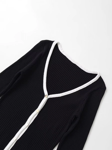 Détail d'un cardigan noir en tricot côtelé avec bordure blanche et boutons dorés