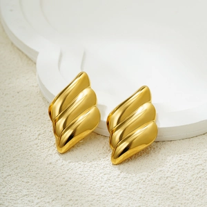 Macro shot of 18K gold wing earrings with a wavy siren texture on a white stone background