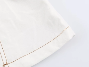 Vue détaillée du tissu en coton blanc avec surpiqûres marron contrastées sur un pantalon
