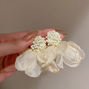 Detail of cream white fabric flower earrings with pearls held by hand for scale