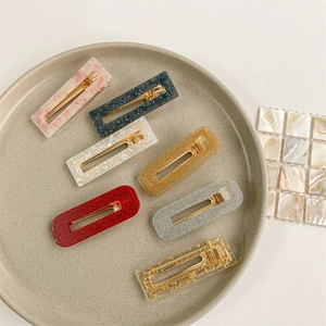 Seven assorted stylish resin and gold glitter hair clips displayed on a ceramic tray