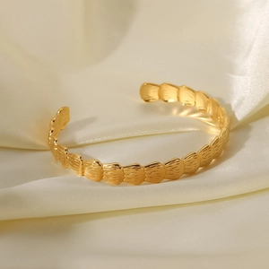 Détail du bracelet rigide en acier titane doré avec texture relief en écailles de poisson