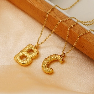 Textured gold lava-style initial necklace with letter B and C pendants on satin fabric