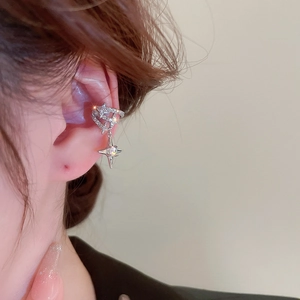 Close-up of silver ear cuff with rhinestone heart and star charms on model's ear