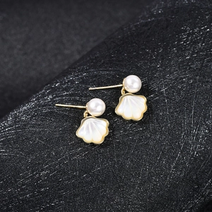 Detailed view of gold shell earrings with white pearls and iridescent mother of pearl texture