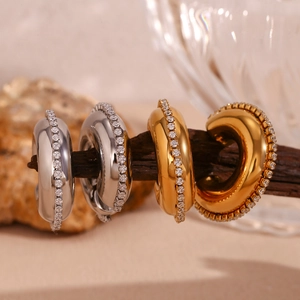 Close-up of gold and silver C-shaped earrings with inlaid zircons on a wooden branch