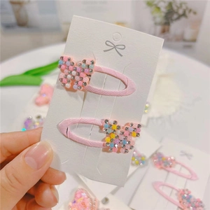 Close-up of pink beaded bow hair clips with rhinestones on a white display card