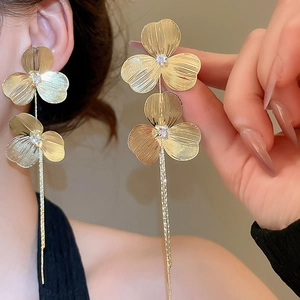Close-up of golden tassel clover earrings featuring zircon inlay and long drop design