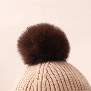 Detail of beige ribbed knit beanie with soft brown faux fur pompom and thick texture