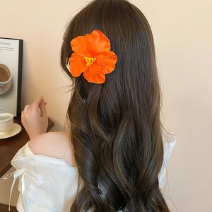Detail view of a large orange hibiscus flower hair clip on wavy brown hair