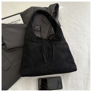 Top view of black suede tote bag with bow tie closure on a textured fabric background