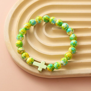 Detail of yellow and green beaded bracelet with a light green cross charm on a tray