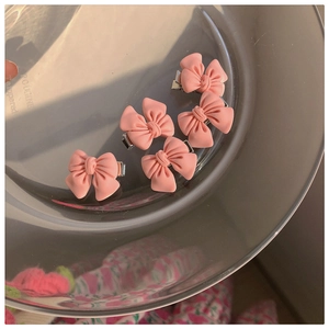 Close-up of five matte pink bow hair clips displayed on a glass tray with soft lighting