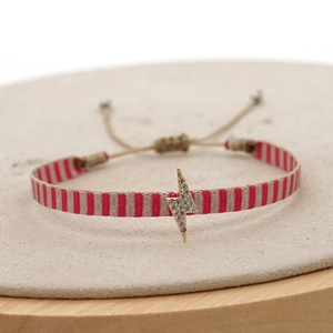 Close-up of woven pink and beige strap bracelet with a gold crystal lightning bolt charm