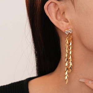 Detailed view of gold leaf tassel earrings with heart-shaped crystal on female model