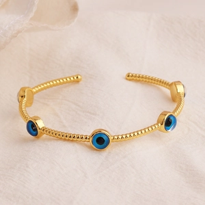 Gold plated open bangle with five blue evil eye charms on beige textured background