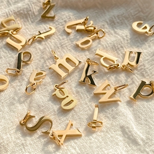 Close-up of gold metal alphabet pendants scattered on a cream textured fabric background