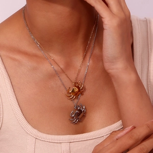 Close-up of gold and silver crab pendant necklaces worn by a model on pink background