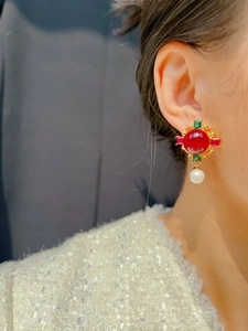 Detail of vintage earring featuring red stone, green crystals, and white pearl drop