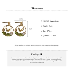 Detailed view of butterfly earrings with green zircon stones and gold hollow circle frame