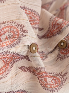 Close-up of metallic gold thread woven into paisley pattern fabric with round brown button
