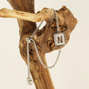 Detail of silver adjustable letter N square pendant on textured natural wood