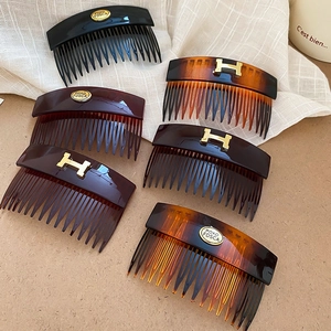 Close-up of vintage oval acrylic hair combs with golden H logo and engraved emblems