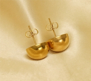 Macro detail of polished gold hemispherical stud earrings on elegant silk background