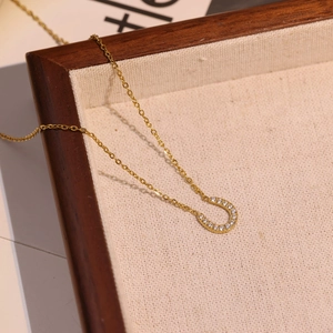 Gold plated U-shape horseshoe necklace with sparkling zircons on a rustic wooden tray