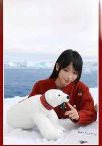 Close-up of fluffy white polar bear plush toy featuring a red plaid scarf in snow scenery