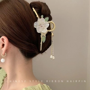 Detail view of floral hairpin with shell-textured petals and long golden pearl tassels