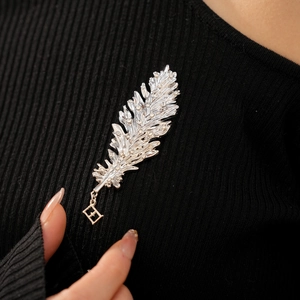 Close-up of a silver feather brooch with sparkling rhinestones and geometric pendant