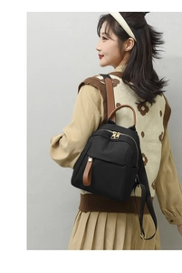 Detail of a chic black Oxford fabric mini backpack with brown leather trim on female model