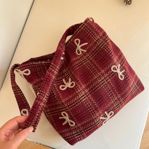 Détail du sac en tissu écossais rouge et noir avec nœud crème et texture en toile vintage