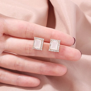Close-up of gold rectangular earrings with white gemstone and pavé crystal border