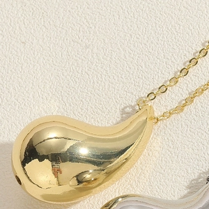 Macro shot of polished gold teardrop pendant on minimalist link chain with smooth finish