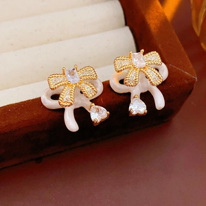 Detailed macro view of bow earrings with gold finish, white enamel, and heart zircon charms