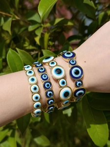 Detailed view of four stacked gold-tone evil eye bracelets with blue and white enamel