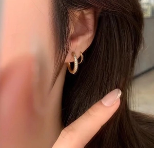 Detail von goldenen Creolen mit glitzernden Zirkonia-Steinen an einem weiblichen Ohr