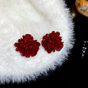 Detailed close-up of dark red layered floral stud earrings on white textured fabric