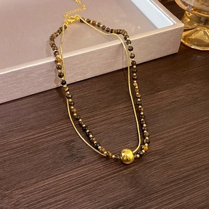 Detail of double-layer necklace with golden snake chain and brown tiger eye beads