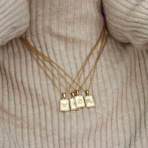 Close-up of four gold layered necklaces featuring white shell zodiac sign pendants
