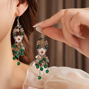 Detailaufnahme der ethnischen Muschelblumen-Ohrringe mit grünen Kristallen am Model